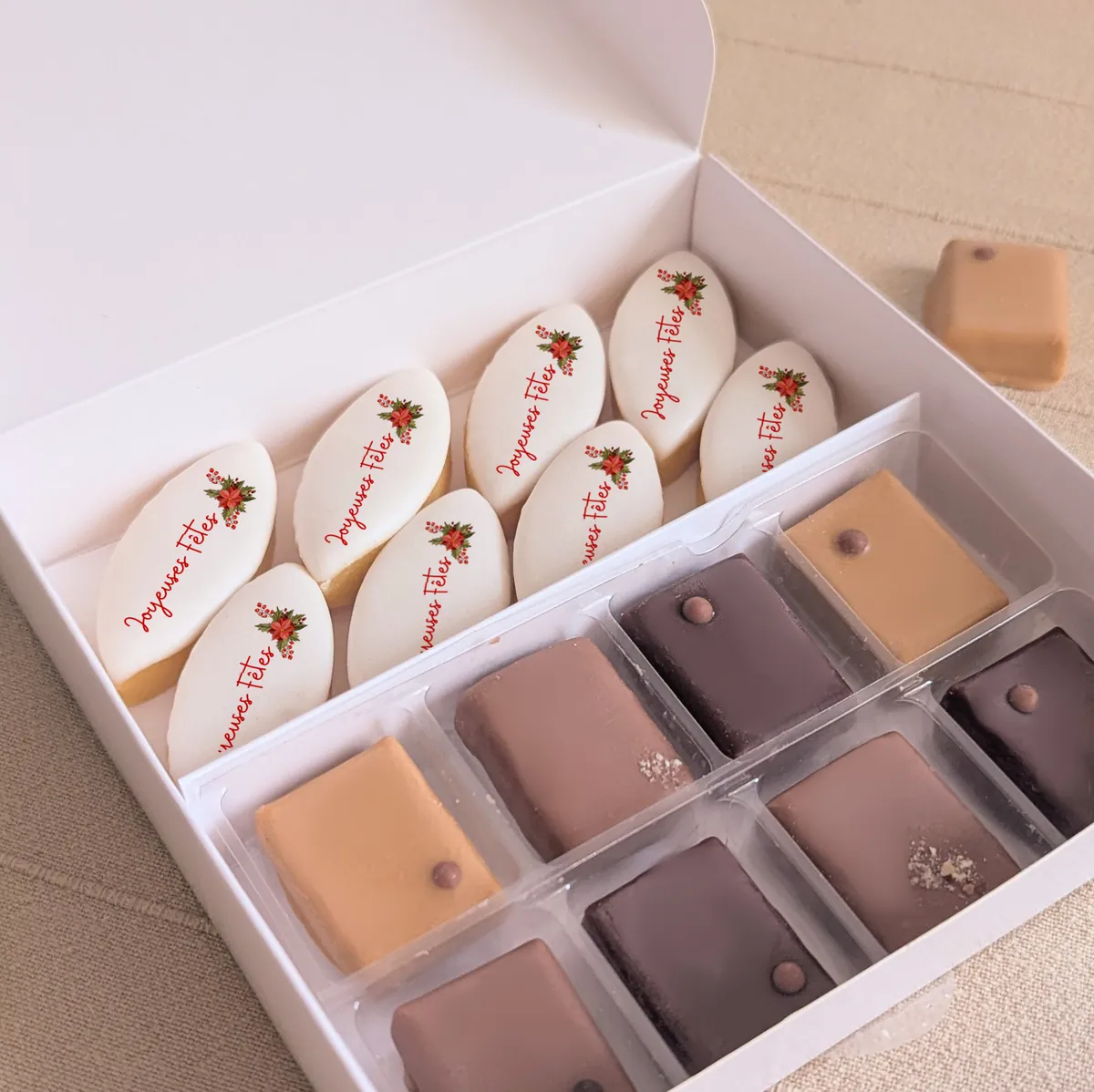 coffret cadeau gourmand noel calissons et chocolats Gros plan sur les calissons personnalisés “Joyeuses Fêtes” et chocolats dans un coffret blanc aux reliefs dorés.