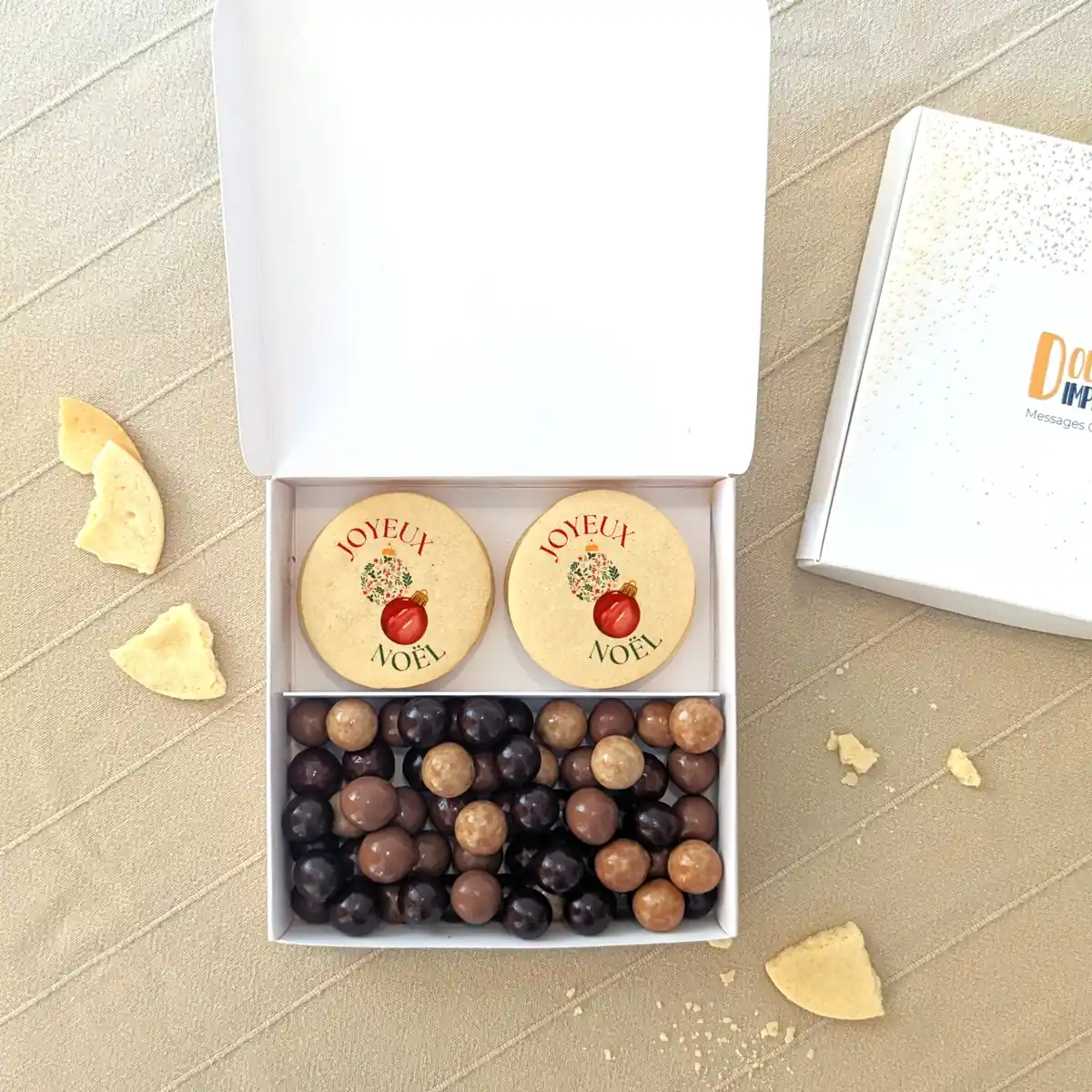 coffret gourmand de noel avec chocolats personnalisés Coffret de Noël avec biscuits “Merry Christmas” et chocolats assortis dans une boîte blanche festive.